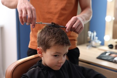 Photo of Professional barber cutting boy's hair in barbershop, closeup