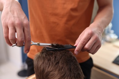 Photo of Professional barber cutting boy's hair in barbershop, closeup