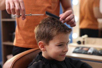 Photo of Professional barber cutting boy's hair in barbershop, closeup
