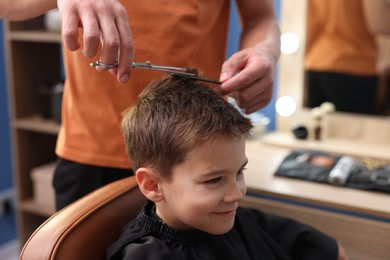 Photo of Professional barber cutting boy's hair in barbershop, closeup