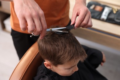 Photo of Professional barber cutting boy's hair in barbershop, above view