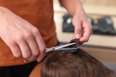 Photo of Professional barber cutting boy's hair in barbershop, closeup