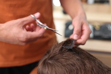 Photo of Professional barber cutting boy's hair in barbershop, closeup