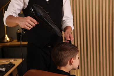 Photo of Professional barber blow drying boy's hair in barbershop, closeup