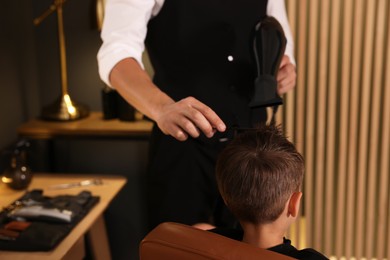 Photo of Professional barber blow drying boy's hair in barbershop, closeup