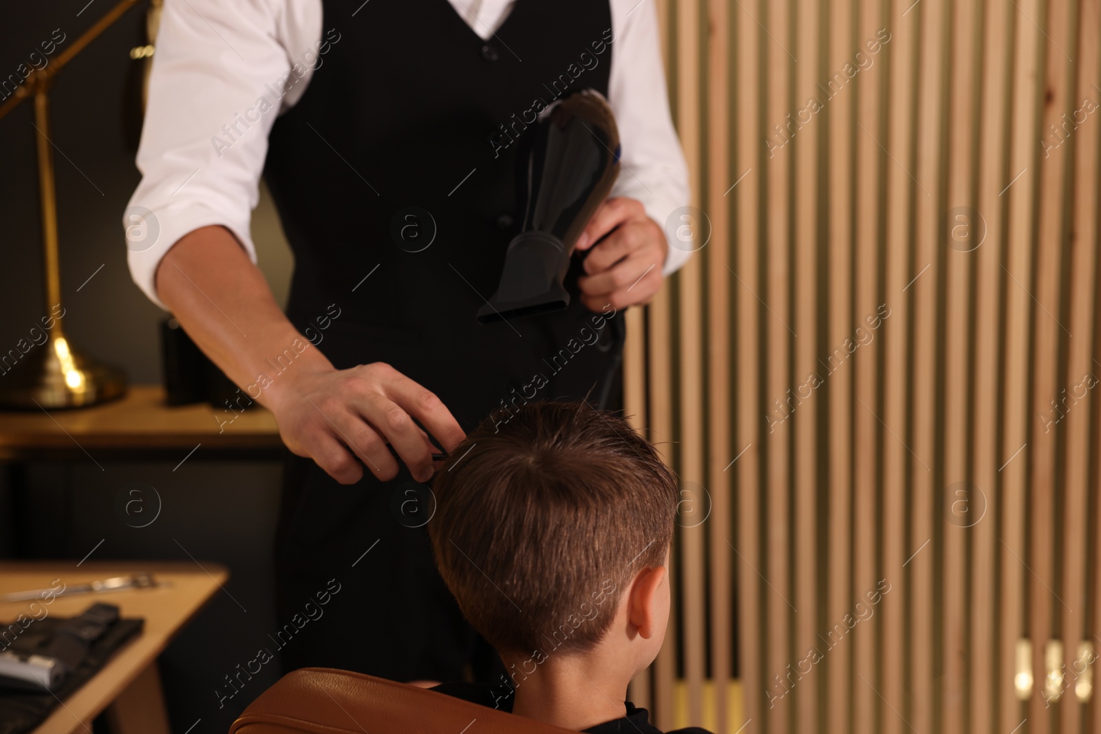 Photo of Professional barber blow drying boy's hair in barbershop, closeup. Space for text