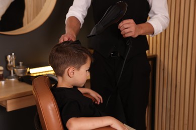 Photo of Professional barber blow drying boy's hair in barbershop, closeup