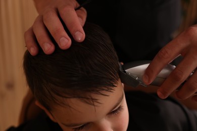 Photo of Professional barber working with little boy in barbershop, closeup