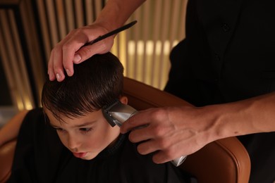 Photo of Professional barber working with little boy in barbershop, closeup
