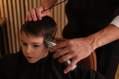 Photo of Professional barber working with little boy in barbershop, closeup