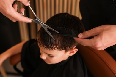 Photo of Professional barber cutting boy's hair in barbershop, above view