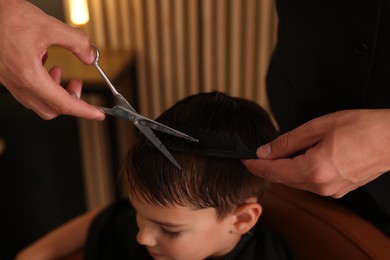 Photo of Professional barber cutting boy's hair in barbershop, closeup