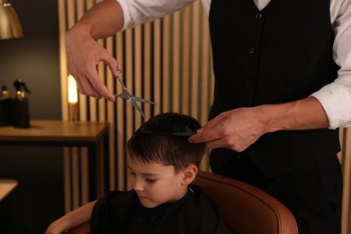 Photo of Professional barber cutting boy's hair in barbershop, closeup