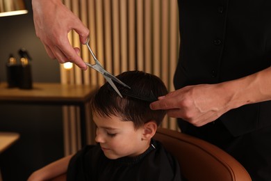 Photo of Professional barber cutting boy's hair in barbershop, closeup