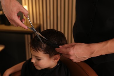 Photo of Professional barber cutting boy's hair in barbershop, closeup