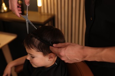 Photo of Professional barber cutting boy's hair in barbershop, closeup