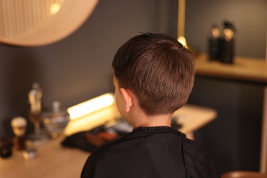 Photo of Cute little boy with cape in barbershop