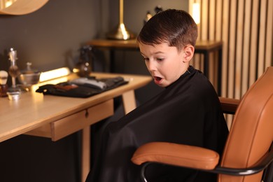 Photo of Cute little boy with cape in barbershop