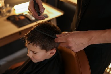 Photo of Professional barber working with little boy in barbershop, closeup
