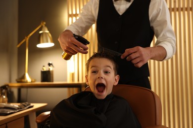 Photo of Professional barber working with little boy in barbershop, closeup