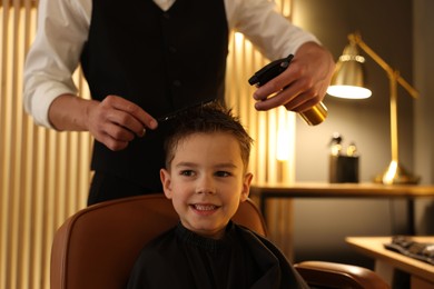 Photo of Professional barber working with little boy in barbershop, closeup