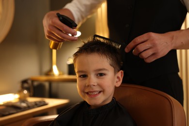 Photo of Professional barber working with little boy in barbershop, closeup