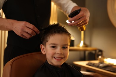 Photo of Professional barber working with little boy in barbershop, closeup