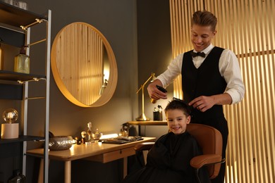 Photo of Professional barber working with little boy in barbershop