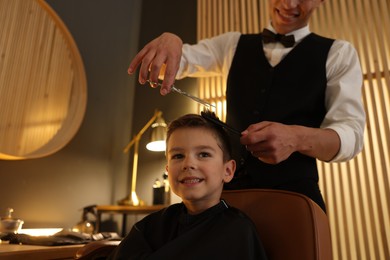 Photo of Professional barber cutting boy's hair in barbershop, closeup