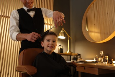 Photo of Professional barber cutting boy's hair in barbershop, closeup