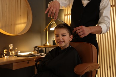 Photo of Professional barber cutting boy's hair in barbershop, closeup