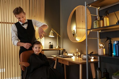 Photo of Professional barber cutting boy's hair in barbershop
