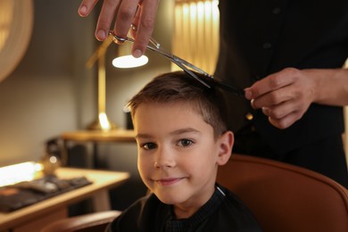 Photo of Professional barber cutting boy's hair in barbershop, closeup. Space for text