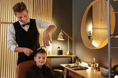 Photo of Professional barber cutting boy's hair in barbershop