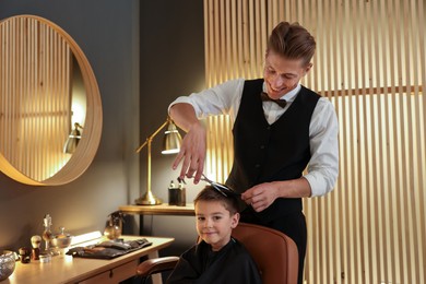 Photo of Professional barber cutting boy's hair in barbershop