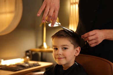 Photo of Professional barber cutting boy's hair in barbershop, closeup. Space for text