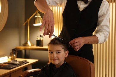 Photo of Professional barber cutting boy's hair in barbershop, closeup