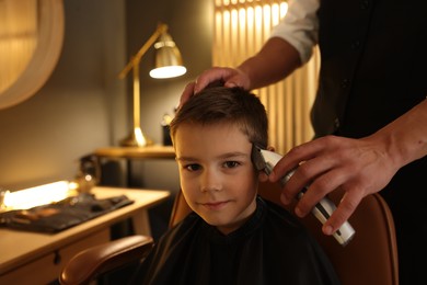 Photo of Professional barber working with little boy in barbershop, closeup