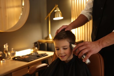 Photo of Professional barber working with little boy in barbershop, closeup