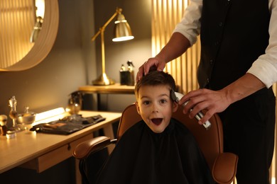 Photo of Professional barber working with little boy in barbershop, closeup