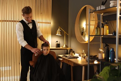 Photo of Professional barber working with little boy in barbershop