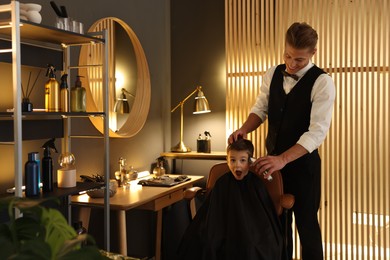 Photo of Professional barber working with little boy in barbershop