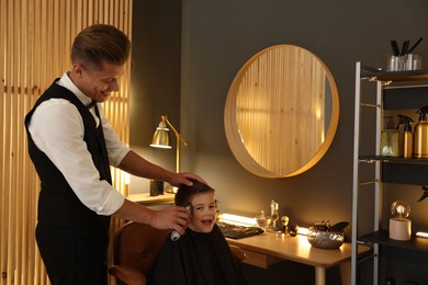 Photo of Professional barber working with little boy in barbershop