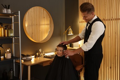 Photo of Professional barber working with little boy in barbershop