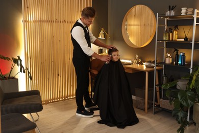 Photo of Professional barber working with little boy in barbershop