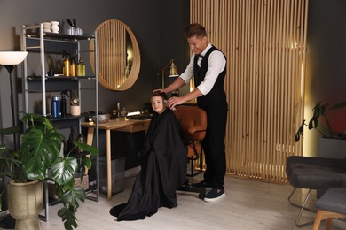 Photo of Professional barber working with little boy in barbershop