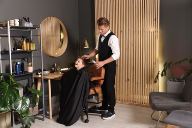 Photo of Professional barber working with little boy in barbershop