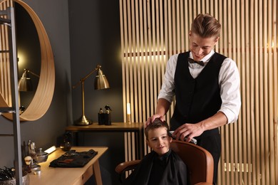 Photo of Professional barber working with little boy in barbershop