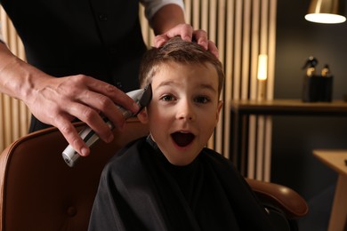 Photo of Professional barber working with little boy in barbershop, closeup