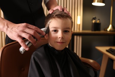 Photo of Professional barber working with little boy in barbershop, closeup